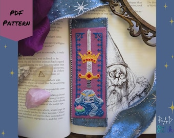 May include: A cross-stitch bookmark with a sword and crown design, featuring a blue bunny with a flower. The bookmark is on a book with a wizard illustration and the text "PDF PATTERN". The bookmark is approximately 20 cm long.