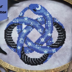 Può includere: Uno schema di punto croce con un design a nodo blu e nero con una mezzaluna e stelle. Lo schema è incorniciato in una cornice dorata.