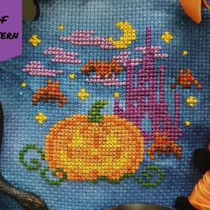 May include: Cross-stitch pattern featuring a Halloween theme. The design includes a large orange pumpkin, bats, a purple castle, a yellow moon, and stars against a blue background. The words "PDF PATTERN" are in a purple banner.