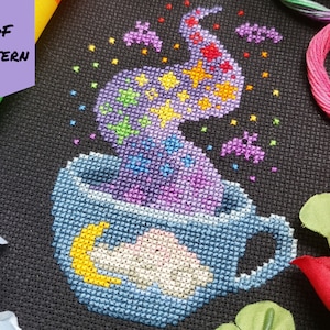 Puede incluir: Patrón de punto de cruz de una taza azul con vapor mágico morado, rosa y amarillo que sale de ella. El vapor está lleno de estrellas, murciélagos y otros elementos mágicos. La taza tiene una nube blanca y una luna creciente amarilla en su interior.