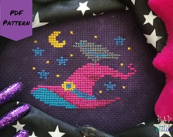May include: Cross-stitch pattern featuring a witch's hat, crescent moon, stars, and a crow against a dark purple background. The words "PDF PATTERN" are in a purple banner. The design is surrounded by a black fabric with white stars.