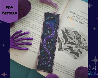 May include: A purple and blue cross-stitch bookmark with a dragon design on a dark gray background. The bookmark is on a book with the text "The Tunnel and the Stars" and "The Trolley House" visible.