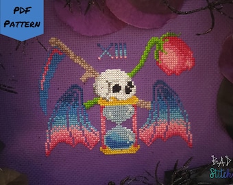 May include: Cross-stitch pattern featuring a skull with an hourglass, wings, and a scythe, with a red rose and the Roman numeral XIII. The design is set against a purple background, with the text "PDF PATTERN".