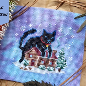 May include: Cross stitch pattern depicting a black cat perched atop a small brown house with a red door. The cat wears a blue collar with a gold bell. The background is a blue and purple gradient with white snowflakes.