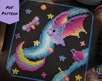 May include: A cross-stitch pattern featuring a dragon on a crescent moon, surrounded by stars and a small planet. The design uses a palette of blues, purples, pinks, and yellows against a black background. The words "PDF PATTERN" are visible.