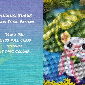 May include: Cross stitch pattern of a white mouse with pink ears and a pink scarf, sitting under a green leaf. The pattern is 76 stitches wide by 78 stitches high and uses 15 DMC colors. Finding Shade Cross Stitch Pattern.