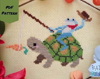 May include: Cross stitch pattern featuring a blue frog riding a green turtle with a carrot on a stick. The pattern is titled "PDF PATTERN" and is from "BAD Stitch".