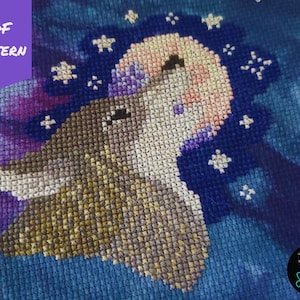 May include: Cross stitch pattern of a wolf howling at the moon with stars in the background. The pattern is on a blue fabric with a purple and pink gradient.