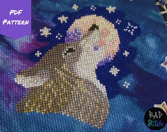 May include: Cross stitch pattern of a wolf howling at the moon with stars in the background. The pattern is on a blue fabric with a purple and pink gradient.