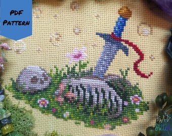 May include: Cross-stitch pattern featuring a sword piercing a skeleton in a grassy scene, with small flowers and a skull. The sword has a blue handle and a red ribbon. The text "PDF PATTERN" is in the upper left corner.
