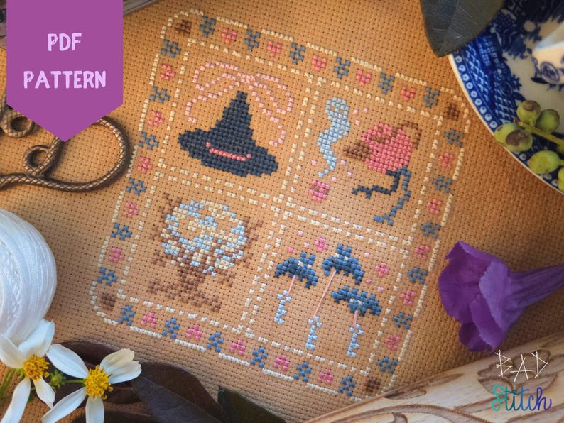 Puede incluir: Patr&oacute;n de punto de cruz con un sombrero de bruja, un fantasma, una flor, una calavera y setas. El dise&ntilde;o est&aacute; enmarcado con detalles en rosa y azul. Las palabras "PDF PATTERN" est&aacute;n en un hex&aacute;gono morado en la esquina superior izquierda.