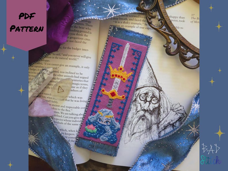 May include: A handmade bookmark with a cross-stitch design featuring a sword, crown, and a blue creature. The bookmark has a pink background with blue trim and the text "PDF PATTERN".