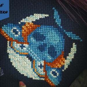 May include: A cross-stitch pattern with a blue and orange fish design on a dark blue fabric. The words "PDF PATTERN" are in the upper left corner. The text "BAD Stitch" is in the lower right corner.