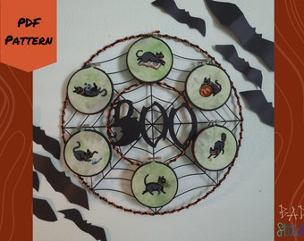 May include: A set of six black cat embroidery hoops with a green background and a black spiderweb design. The hoops are arranged in a circle and the word "BOO" is written in black letters in the center. The hoops are hanging on a white wall with black bats.