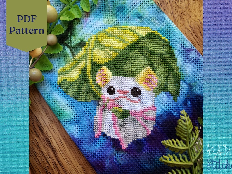 May include: Cross stitch pattern featuring a white mouse wearing a green and yellow leaf hat. The mouse is surrounded by a blue and purple watercolor background. The pattern is labeled "PDF Pattern".