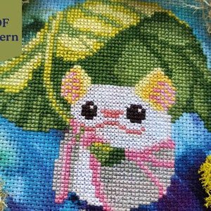 May include: Cross stitch pattern featuring a white cat with pink ears and a green leaf hat. The cat is wearing a pink scarf and is surrounded by a blue and green background.