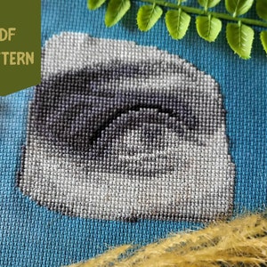 Peut inclure: Un motif de point de croix représentant un nuage gris et noir sur un fond bleu. Le motif est encadré par une bordure blanche.