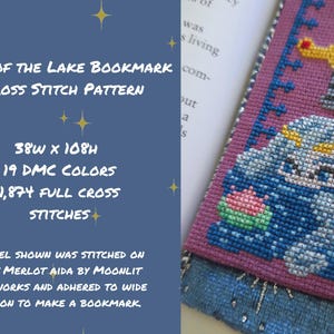 May include: Cross-stitch bookmark featuring a design of the Lady of the Lake with a sword. The bookmark is stitched on a purple background with blue and white details. The text on the left side reads "Lady of the Lake Bookmark Cross Stitch Pattern".