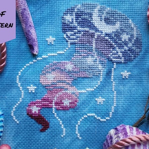May include: A cross-stitch pattern of a purple and pink jellyfish with white stars on a blue background. The pattern is labelled "PDF PATTERN".