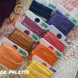 May include: A collection of colorful embroidery floss spools in shades of orange, yellow, pink, purple, and teal. Each spool is labeled with a number. The text "COLOR PALETTE" is visible at the bottom. The image is on a patterned surface.