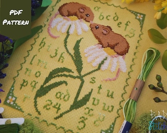 May include: Cross stitch pattern featuring two brown mice on a yellow background with white daisies and green leaves. The pattern includes the alphabet and numbers.