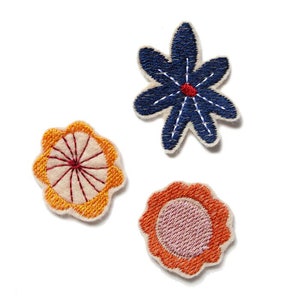 Könnte beinhalten: Drei gestickte Stoffblumen-Patches. Einer ist blau mit roter Mitte, einer ist orange mit roter Mitte und einer ist rosa mit orangefarbener Mitte.