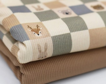 Puede incluir: Una pieza de tela acanalada doblada con un patrón de cuadros en crema, beige, verde salvia y azul pizarra. Algunos cuadros contienen pequeñas ilustraciones de animales del bosque, incluyendo un ciervo, un conejo y un koala. Debajo hay una tela acanalada marrón sólida.