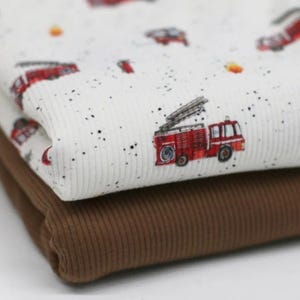 May include: Two pieces of fabric, one white with a red fire truck pattern and black speckles, and the other brown. Both fabrics have a ribbed texture.