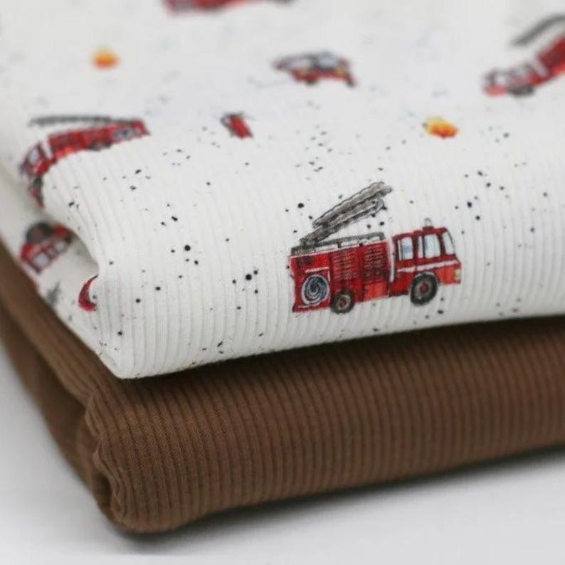 May include: Two pieces of fabric, one white with a red fire truck pattern and black speckles, and the other brown. Both fabrics have a ribbed texture.