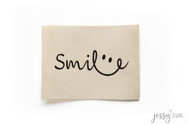 May include: A beige fabric label with the word "Smile" written in black cursive with a smiley face drawn next to it.