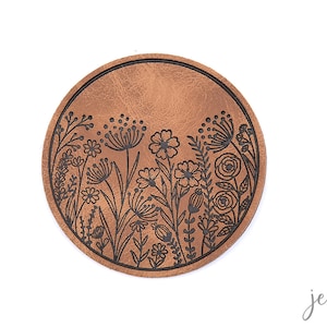 Könnte beinhalten: Ein runder brauner Lederuntersetzer mit einem schwarzen Blumenmuster. Das Design zeigt eine Vielzahl von Blumen und Blättern.