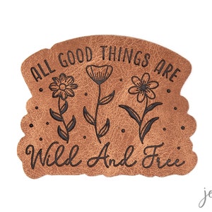 Könnte beinhalten: Ein braunes Leder-Patch mit dem Text "All good things are wild and free" und drei stilisierten Blumenillustrationen.