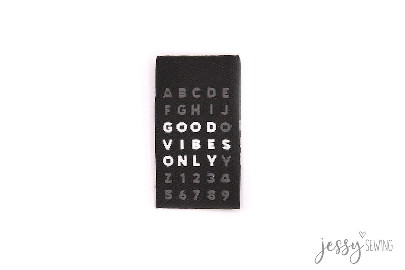 Puede incluir: Etiqueta de tela negra con texto blanco que dice "GOOD VIBES ONLY" rodeada de letras del alfabeto y n&uacute;meros del 0 al 9.