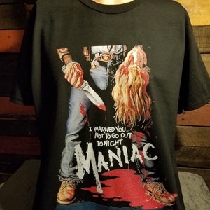 May include: Black t-shirt with a graphic print of a man holding a knife and a severed head. The graphic is from the horror movie "Maniac" and includes the text "I warned you not to go out tonight Maniac".