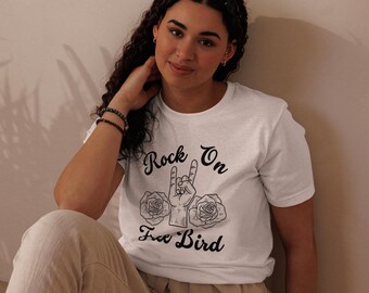 Könnte beinhalten: Ein weißes Kurzarm-T-Shirt mit einem schwarzen Grafikdruck einer Hand, die eine Rock-and-Roll-Geste macht, flankiert von zwei Rosen. Der Text "Rock On" steht über der Hand und "Free Bird" darunter in schwarzer Schreibschrift.