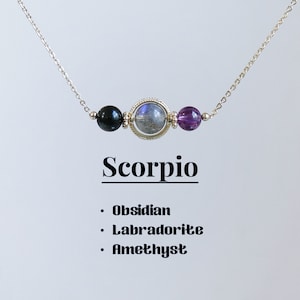 May include: A silver chain necklace with three gemstone beads: black obsidian, iridescent labradorite, and amethyst. The necklace is labelled "Scorpio: Obsidian, Labradorite, Amethyst".
