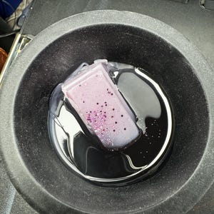 May include: A purple candle with glitter embedded in the wax is melting in a black metal container.