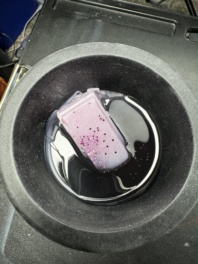 May include: A purple candle with glitter embedded in the wax is melting in a black metal container.
