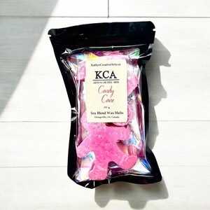 May include: Pink soy wax melts shaped like people, packaged in a clear plastic bag with a black label that reads "KCA Kathy's Creative Arts Candy Cane 103 g Soy Blend Wax Melts Orangeville, ON, Canada"