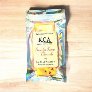 Op de afbeelding: Een klein pakketje sojawas smelt in een doorzichtige plastic zak. De was smelt is geel en heeft een label met de tekst "KCA Kathy's Creative Arts Pumpkin Pecan Cheesecake 43 g Soy Blend Wax Melts Orangeville, ON, Canada".