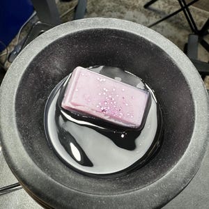 May include: A purple wax melt with glitter is melting in a black wax warmer.