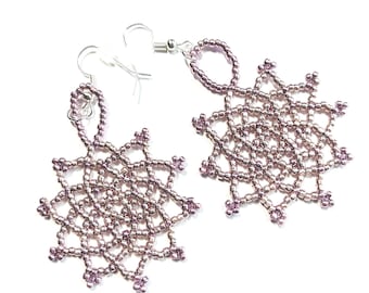 May include: A pair of handmade beaded earrings. The earrings have a delicate, openwork design in a soft, muted pink colour. The intricate pattern resembles a star or snowflake, with small beaded accents.