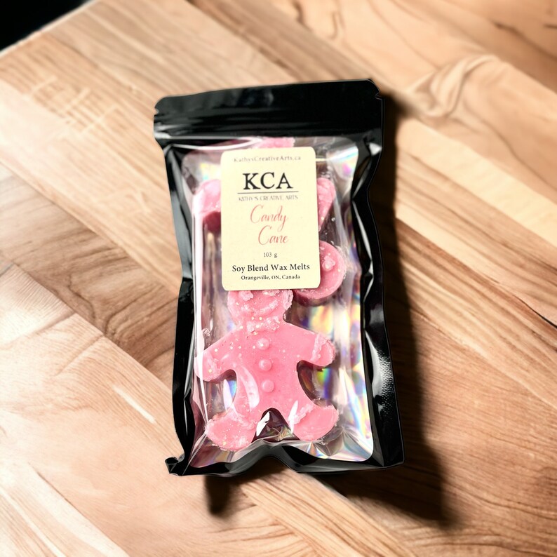 May include: A package of pink soy wax melts shaped like a gingerbread person. The package is labeled "KCA Candy Cane Soy Blend Wax Melts 103 g Orangville, ON, Canada".