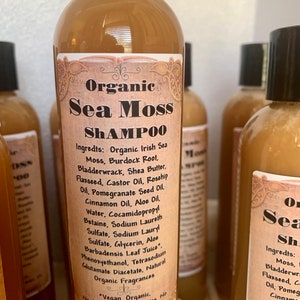 May include: A collection of brown bottles of Organic Sea Moss Shampoo with black caps. The labels list ingredients like Irish Sea Moss, Burdock Root, and Aloe Oil. The text on the label also states that the shampoo is vegan, organic, and paraben-free.