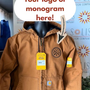 May include: A tan hooded jacket with a front zipper, black interior lining, and two front pockets. A circular black patch with a gear border, crossed wrenches, and the letters 2, 3, and T is on the chest. Yellow Carhartt tags are attached.
