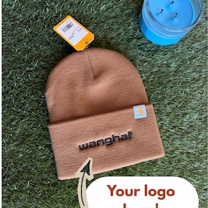 May include: A brown knit beanie with a folded cuff featuring the embroidered text "wanghaf" in dark thread and a small white Carhartt brand tag. An orange product tag is attached to the top, and a white graphic overlay reads "Your logo here!"