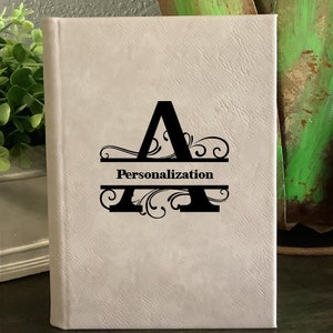 May include: A white leather-bound journal with a black letter "A" and decorative flourishes. The text "Personalization" is printed on a black line above the letter.