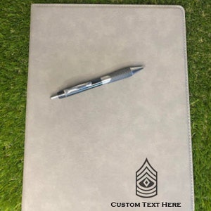 May include: A gray leatherette folder with a black pen and a black and white insignia of a military rank. The text "CUSTOM TEXT HERE" is printed below the insignia.