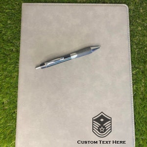 May include: A gray leatherette folder with a black pen on top. The folder has a black insignia with a star and three stripes, and the text "CUSTOM TEXT HERE" is printed below the insignia.