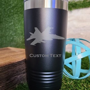 May include: A black stainless steel tumbler with a silhouette of a fighter jet and the text "CUSTOM TEXT".